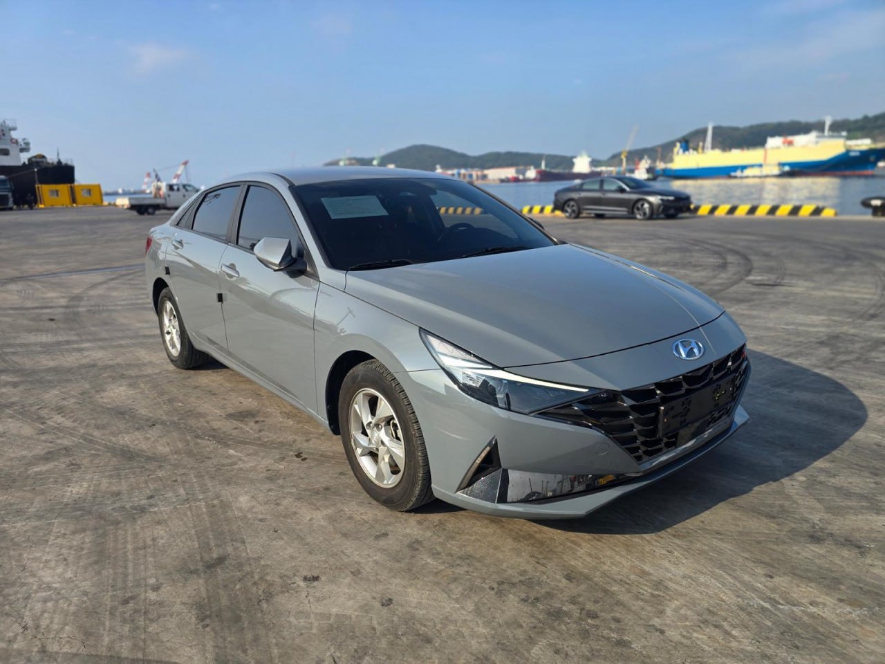 Grey Hyundai Avante on the quay, with the sea and vessels in the background